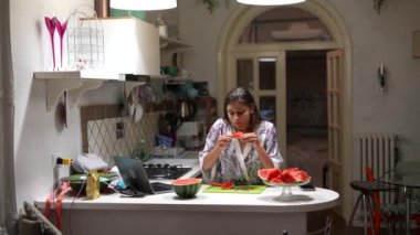 Bir kadın mutfak atmosferinde yemek kesmekle meşgul ve tezgahın yanına bir karpuz yerleştirilmiş.