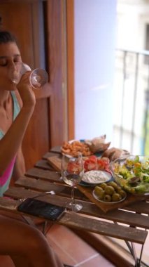 Konforlu bir balkon kahvaltı sahnesi. İçinde şarap, taze salata, deniz ürünleri ve küçük ahşap bir masada aperatifler var..