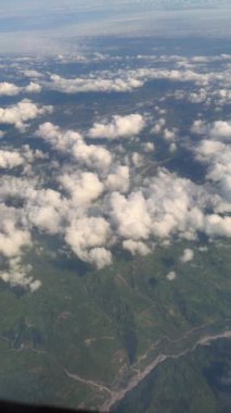 Bir uçak penceresinden görülen canlı yeşil manzaranın üzerinde süzülen beyaz bulutların nefes kesici bir hava perspektifi.