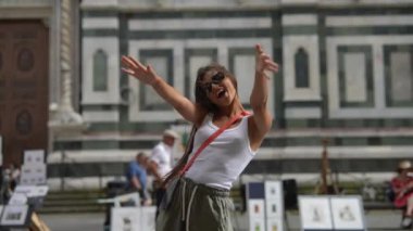 Güneş gözlüklü genç bir kadın tarihi bir binanın önünde poz veriyor, şehir ortamında neşe gösteriyor.