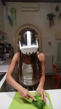 Modern bir mutfakta sebze doğrarken, teknoloji ve yemekleri birleştirirken VR kulaklık kullanan bir kadın..