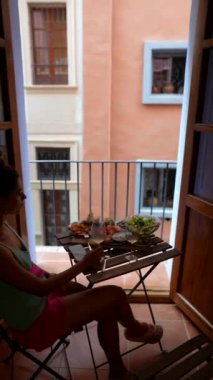 Şehirde, bir kadın rahat balkonda sakin bir sabah geçirir, manzaralı kahvaltısının tadını çıkarır.