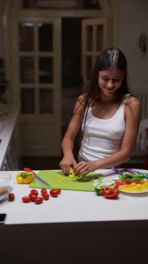 Moda bir mutfakta, genç bir kadın renkli biberler ve domateslerle canlı sebzeler doğruyor.