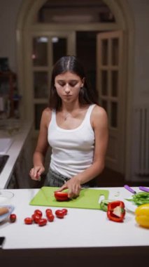 Günümüz mutfağında, beyaz atletli genç bir kadın besleyici bir yemek hazırlamak için sebze doğruyor.