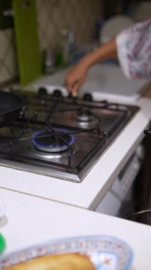 Modern bir mutfakta, bir insan mavi bir alevle gaz ocağında yemek pişiriyor, mutfak becerileri ve verimliliği gösteriyor.