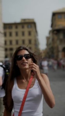 Bir şehirde, güneş gözlüklü şık bir bayan ve beyaz bir atlet modaya uygun bir şehir aurasına sahiptir.
