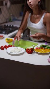 Beyaz kolsuz tişörtlü bir kadının, mutfakta sağlıklı bir salata hazırlamak için malzemeleri dilimlerken yakın çekimi..