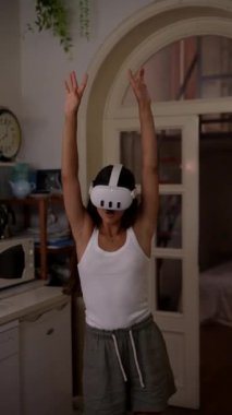 Bir kadın rahat bir oturma odasında VR kulaklığı takarken mutlu bir şekilde dans ediyor ve eğleniyor.