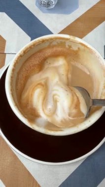 Tamamlanmamış bir fincan kahvenin havadan bir perspektifi, bir kaşıkla, şık geometrik desenli bir masa üzerinde düzenlenmiş.