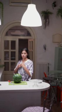Modern mobilyalar ve tezgahın üstünde karpuzla çevrili, rahat bir mutfakta telefonla konuşan bir kadın..