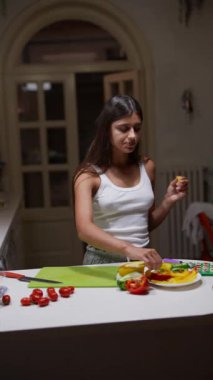 Beyaz atletli genç bir kadın modern bir mutfakta taze sebzelerle sağlıklı bir yemek hazırlıyor..