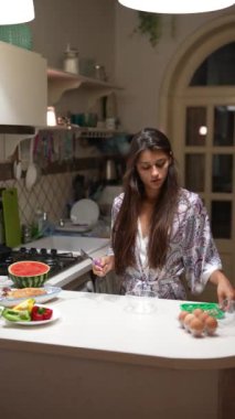 Geceleri modern bir mutfakta taze meyve ve sebzelerle sağlıklı bir kahvaltı hazırlayan bir kadın..