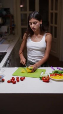 Genç bir kadın, modern bir mutfakta yeşil bir kesme tahtasının üzerinde muz dilimlemeye odaklanır ve sağlıklı bir yemek hazırlar.