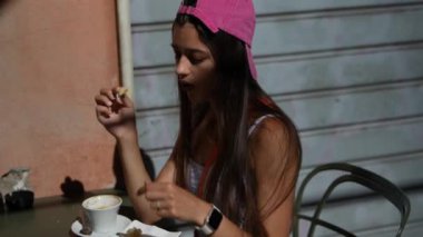 Pembe şapkalı ve akıllı genç bir bayan güneşli bir günde, açık havada bir kafe masasında dondurmanın içinde keyif çatıyor.