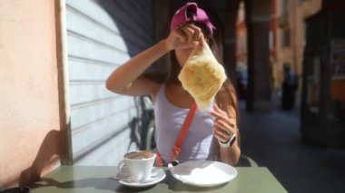 Bir kadın güneşli bir günde şehrin güzel bir kaldırım kafesinde lezzetli bir hamur işi ve kahvenin tadını çıkarıyor.