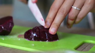 Yeşil kesme tahtasındaki taze pancarları doğrayan kişi, yemek pişirmek için gerekli malzemeleri özenle hazırlıyor..