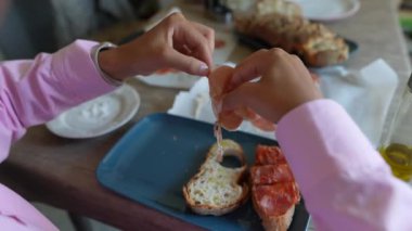 Ekmek, peynir ve domatesle kahvaltıyı hazırlayan elleri gösteren yakın plan bir çekim.