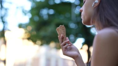 Bir kadın kablosuz kulaklık takıp, arka planda yeşil yapraklı bisküvi yemekten hoşlanır..