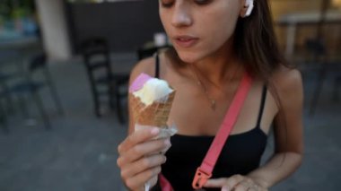 Kulaklık takan genç bir kadın dışarıda dondurma külahı yerken mutlu bir şekilde rahat ve rahat bir anı yakalıyor.