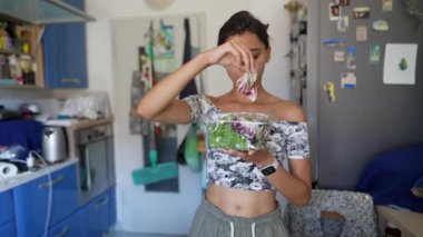 Genç bir kadın, çağdaş bir mutfakta mavi dolaplar ve çeşitli mutfak malzemeleriyle taze salata yapıyor..