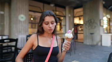 Genç bir kadın canlı bir şehir ortamında müziğin tadını çıkarırken dondurma külahının tadını çıkartıyor.