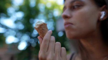 Bir kadın dışarıda kablosuz kulaklıklarla dondurma yiyor. Dinlenme ve teknoloji deneyimini geliştiriyor.
