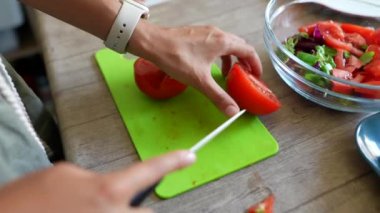 Mutfaktaki yeşil kesme tahtasıyla taze domatesleri dilimleyen ellerin yakın çekimi..