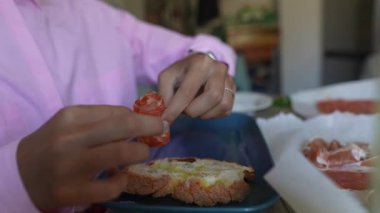 Mutfakta bir kadın elleriyle taze ekmek ve malzemelerle sandviç yapıyor.