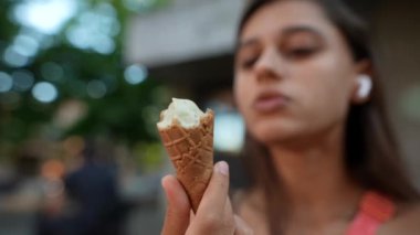 Şehir parkında, kulaklıklı genç bir kadın vanilyalı dondurmanın tadını çıkarıyor, bir anlık mutluluğu yakalıyor.