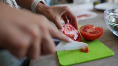 Mutfaktaki yeşil bir kesme tahtasıyla taze domatesleri seramik bir bıçakla doğrayan birinin yakın çekimi..