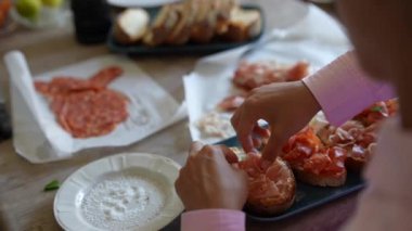 Bir insan masandaki çeşitli malzemelerle ustalıkla sandviç hazırlıyor ve mutfak sanatını sergiliyor.