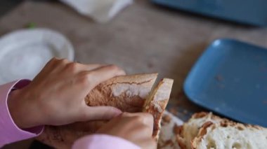 Arka planda mavi bir tabak ve tabakla taze ekmek parçalayan ve yiyen bir kişinin yakın plan görüntüsü..
