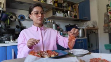 Mavi dolaplı temiz bir mutfakta, genç bir kadın mutlu bir şekilde pizza yer ve rahat bir atmosfer yaratır.