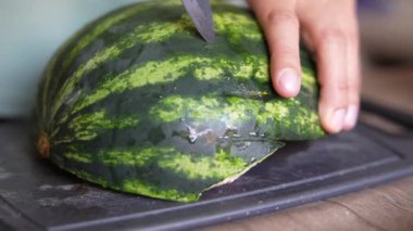 Kesme tahtasında karpuz kesen ellerin yakın plan görüntüsü taze ve sulu meyve sunar.
