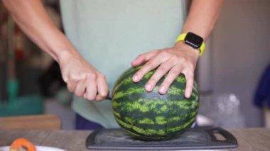 Modern bir mutfakta kesme tahtasıyla karpuz kesen, akıllı seğiren ellerin yakın çekimi..