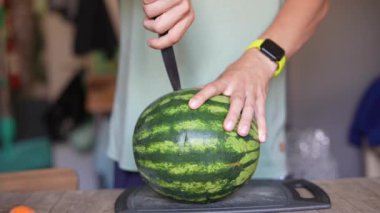 Mutfak ortamında karpuzu bıçakla kesen birinin yakın çekim görüntüsü.