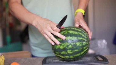 Bir insanın mutfak tezgahında karpuz dilimlerken yakın plan fotoğrafı. Bıçak kullanıyor, sarı bir akıllı yama takıyor..