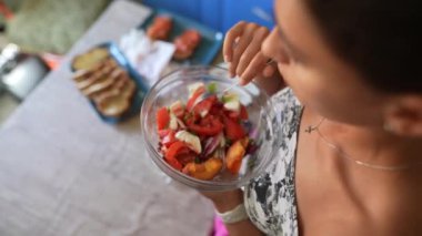 Sağlıklı sebze salatasının tadını çıkaran bir kadın. Mutfakta duruyor. Yanında taze malzemelerle..