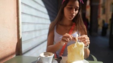 Sıcak bir içecek ve hamur işi de dahil olmak üzere kahvaltısının tadını çıkaran genç bir kadın..