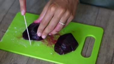 Mutfakta, eller, vejetaryen yemeği hazırlamak için ahşap bir kesme tahtasındaki renkli taze pancarları dilimlemeye odaklanır.