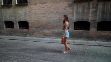 Modayı takip eden genç bir kadın sakin bir şehir sokağında rahatça dolaşır, stil ve özgüven saçar.