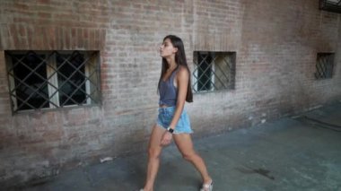 Genç bir kadın zarif bir şekilde canlı, tuğlalı bir sokak arasında yürüyor, modern sokak tarzını somutlaştırıyor.