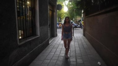 Genç bir kadın sakin bir şekilde hoş ve büyüleyici bir şehir sokağında yürüyor, yumuşak bir akşam ışığı ile kaplanmış.