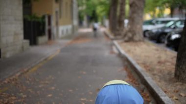 Huzurlu ve huzurlu bir sokakta, yemyeşil ağaçlar ve park halindeki arabalarla rahatça gezinen bir insan.