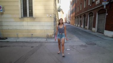 Genç bir kadın güneşli bir caddede sakin bir şekilde yürüyor, hayat dolu şehir hayatının özünü tamamen yakalıyor.