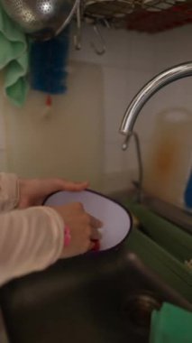 Eller, mutfak lavabosunda bir kâseyi özenle yıkıyor ve çeşitli günlük ev işlerini etkili bir şekilde gösteriyor.