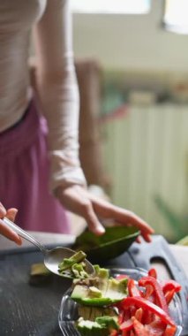 Bir insan, sıcak ve davetkar bir mutfakta renkli taze sebzeler hazırlarken bir avokadoyu ustalıkla tutar.