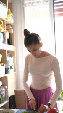 Yetenekli bir kadın sağlıklı yemekler hazırlar, modern mutfağında canlı sebzeleri en son aletlerle doğrar.