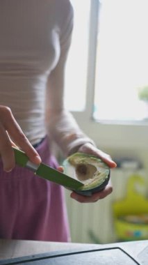 Parlak ve davetkar bir mutfak alanında, bir kadın ustalıkla ve ustalıkla bir avokadoyu kesiyor.