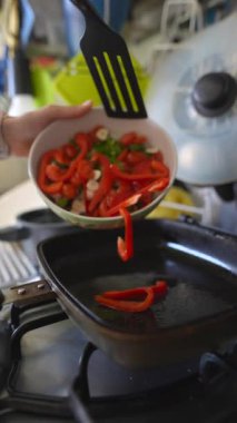 Canlı ve taze kırmızı dolma biberler lezzetli bir kızartma yemeği yapmak için sıcak tavaya ustalıkla ekleniyor.